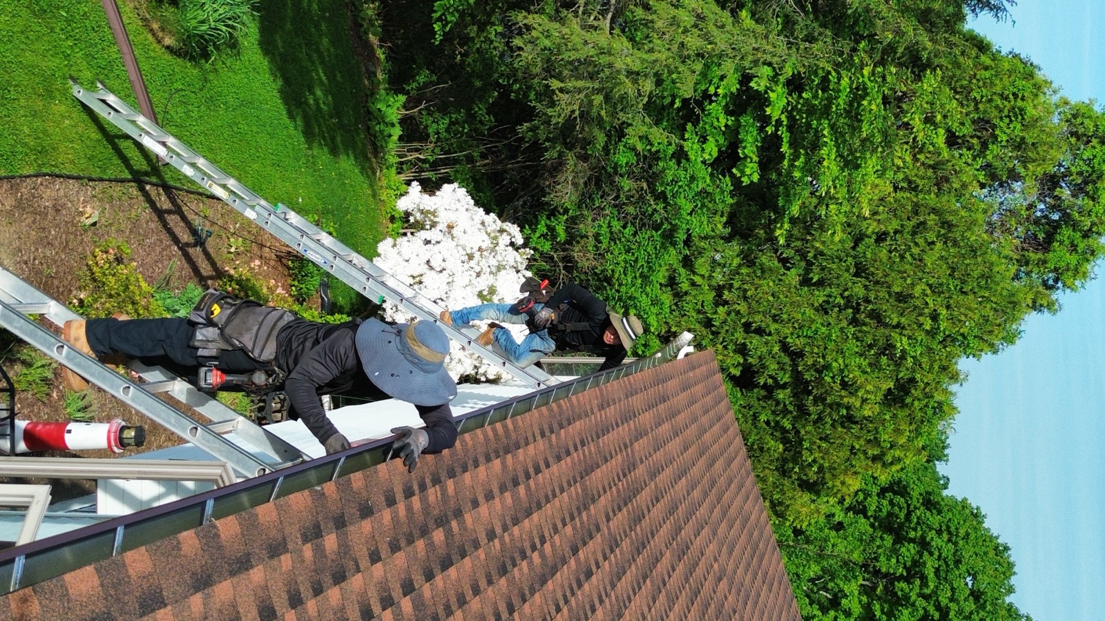 JML Construction crew on a ladder working a warm-brown architectural shingle roof surrounded by Connecticut trees